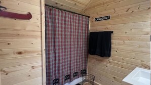 Baño de cabaña con cortina de ducha escocesa, un lavamanos blanco y suelo de madera.