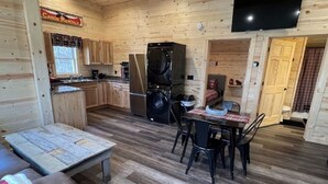 Interior de una cabaña con comedor, cocina y televisor montado en la pared.