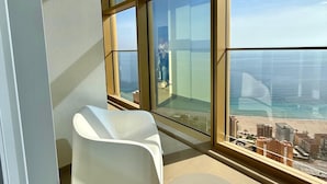 A balcony with a white chair and a small table, overlooking a beach and cityscape. - Intempo Spa (Benidorm)