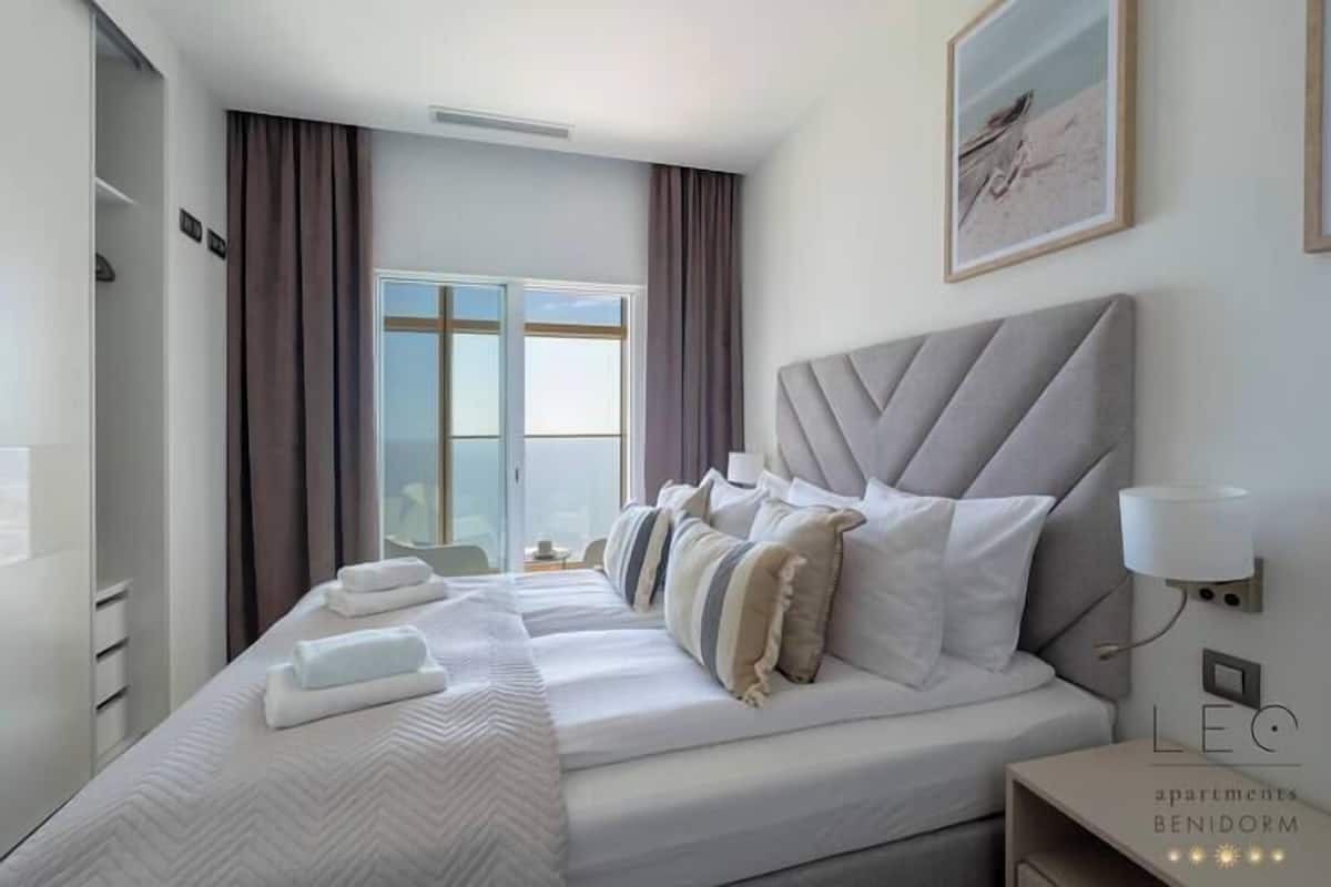 A hotel room with a large bed, a bedside table, a lamp, and a window with curtains.