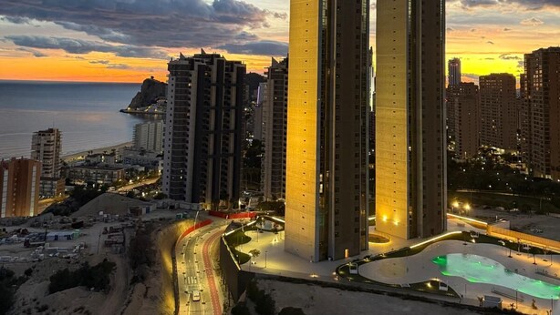 A high-rise building with a unique curved top, surrounded by other tall buildings, a curved road, and a body of water in the background. - Intempo Spa (Benidorm)