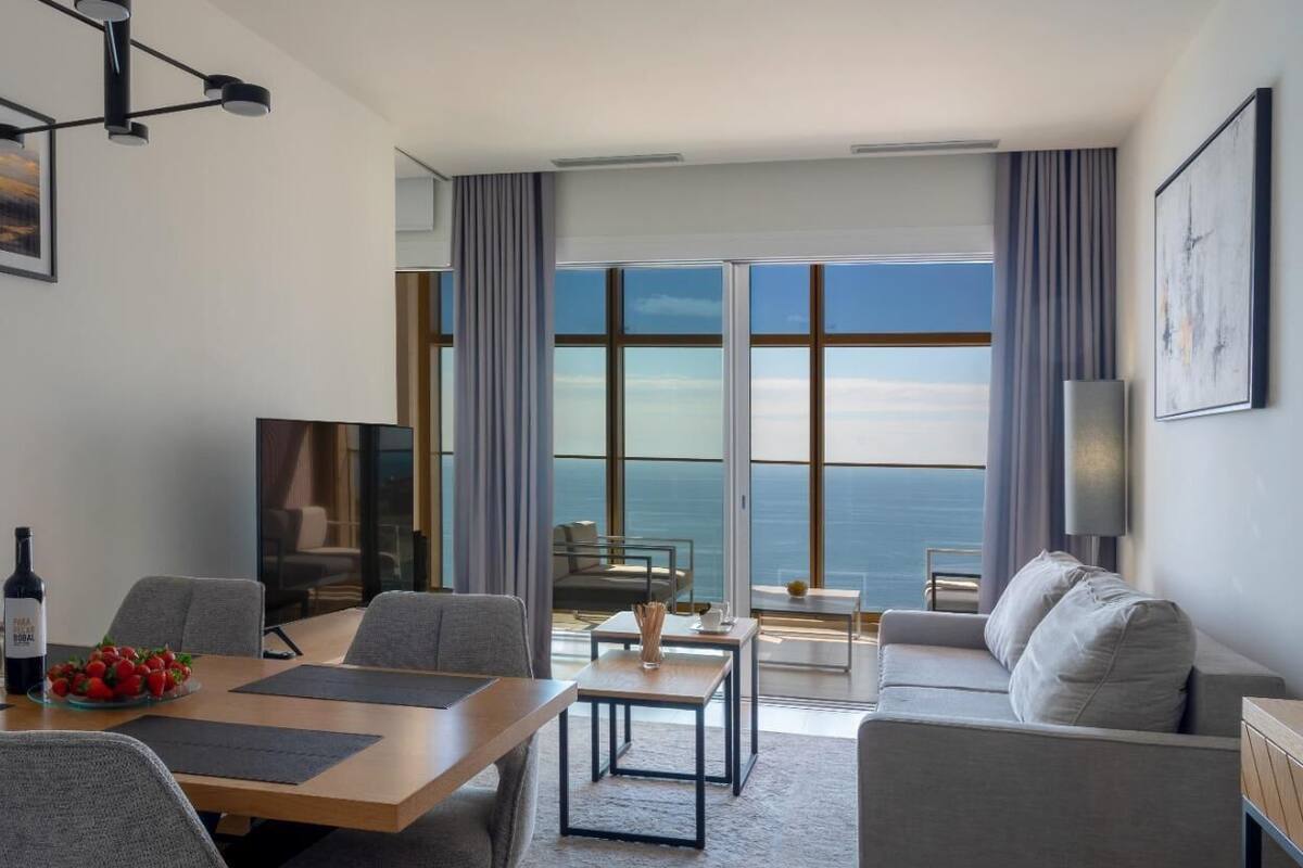A modern hotel room with a dining area, a sofa, and a view of the ocean.