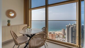 A balcony with a view of the ocean and cityscape, featuring wicker chairs, a round table, and a pineapple on the counter. - Intempo Spa (Benidorm)