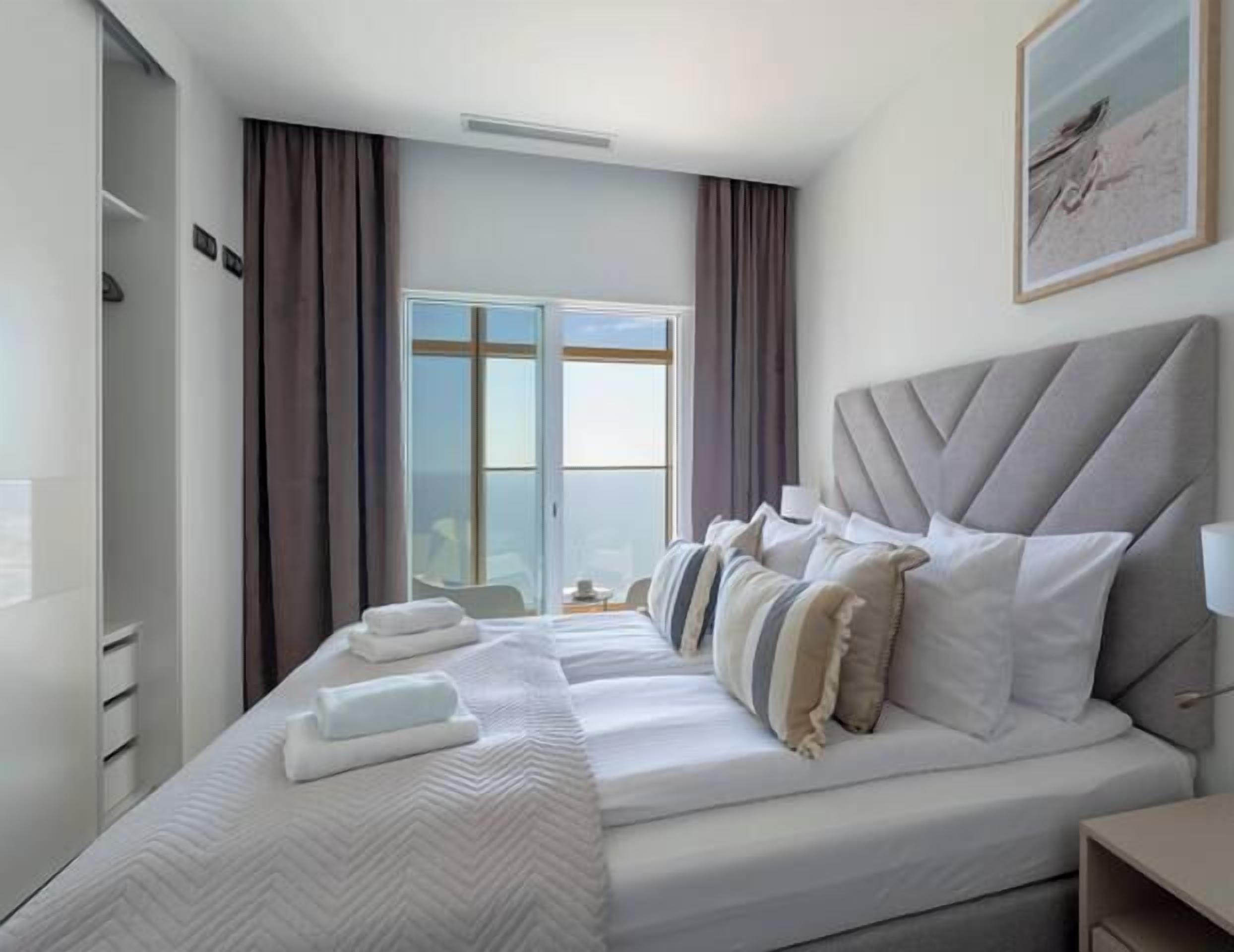 Une chambre d’hôtel avec un grand lit, une table de chevet, une lampe et une fenêtre avec des rideaux.
