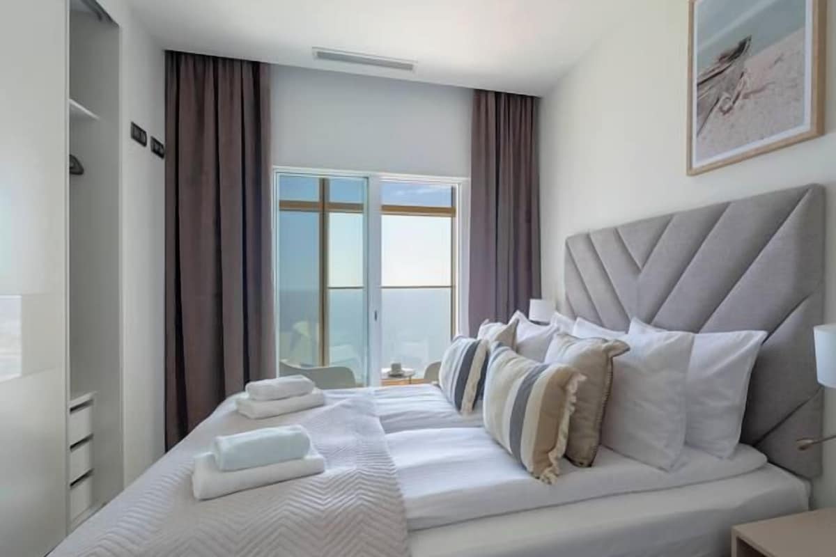 A hotel room with a large bed, a bedside table, a lamp, and a window with curtains.