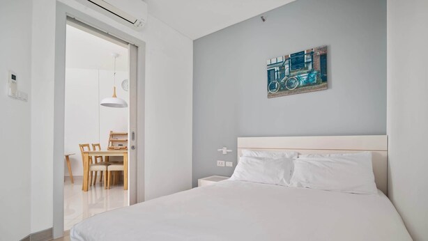 A modern bedroom with a large bed, a dining area with a table and chairs, and a wall-mounted bicycle painting. - Cassia Residences, Two-Bedroom C Deluxe Lake (Choeng Thale)