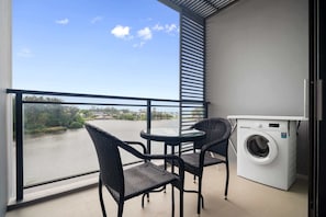 Un balcon équipé d’un lave-linge, de deux fauteuils en osier et offrant une vue sur une rivière.