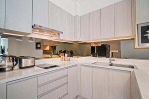 A modern kitchen with light wood cabinets, a white countertop, a built-in oven, and a coffee maker.