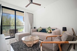 A modern living room with a glass coffee table, a sofa, a chair, and a ceiling fan.