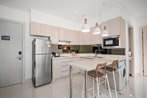 Une cuisine moderne dotée d’appareils électroménagers en acier inoxydable, d’un îlot central avec des tabourets de bar, d’un éclairage suspendu et d’un micro-ondes encastré.