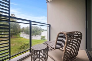 A balcony with a wicker chair and a small round table, overlooking a river and greenery.