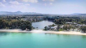 An aerial view of a coastal resort with a large body of water, a sandy beach, and a dense cluster of buildings. - Cassia Residences, One Bedroom A Ground Floor (Choeng Thale)