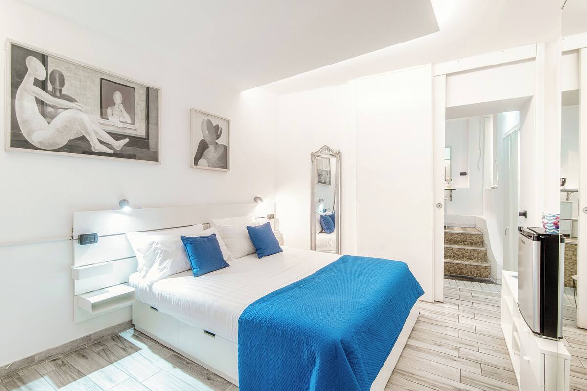 A modern bedroom with a bed, bedside tables, a mirror, and artwork on the wall.