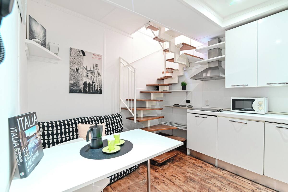 A compact kitchen with white cabinetry, a microwave, and a wooden staircase.