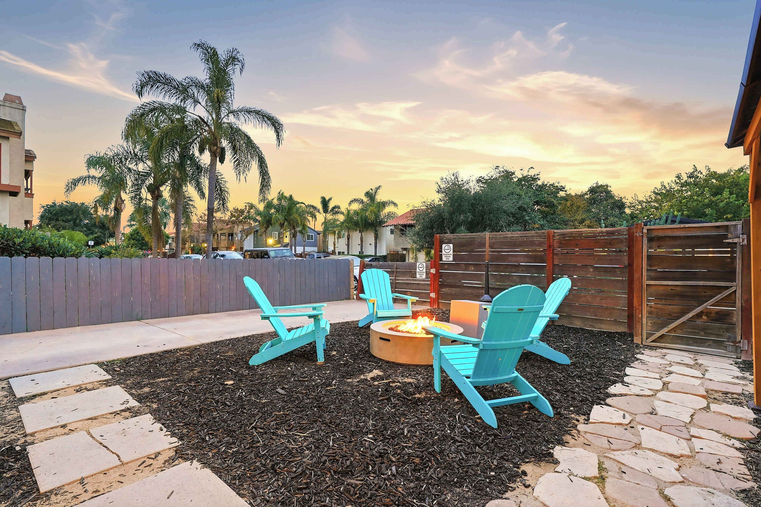 An outdoor patio area with a fire pit and turquoise chairs, surrounded by mulch and stone tiles.