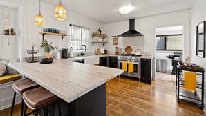 A modern kitchen with a central island, pendant lights, and wooden flooring.