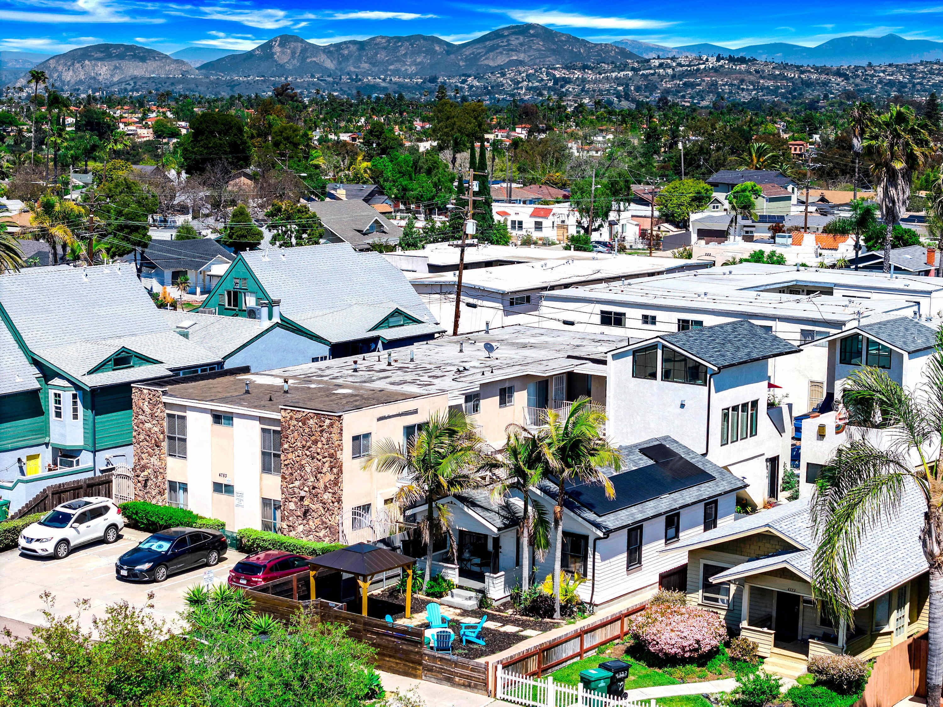 A residential area with houses, a parking lot, and a mountain range in the background.