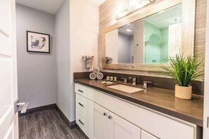 Un baño moderno con un espejo grande, armarios blancos, una encimera beige y una planta en maceta.