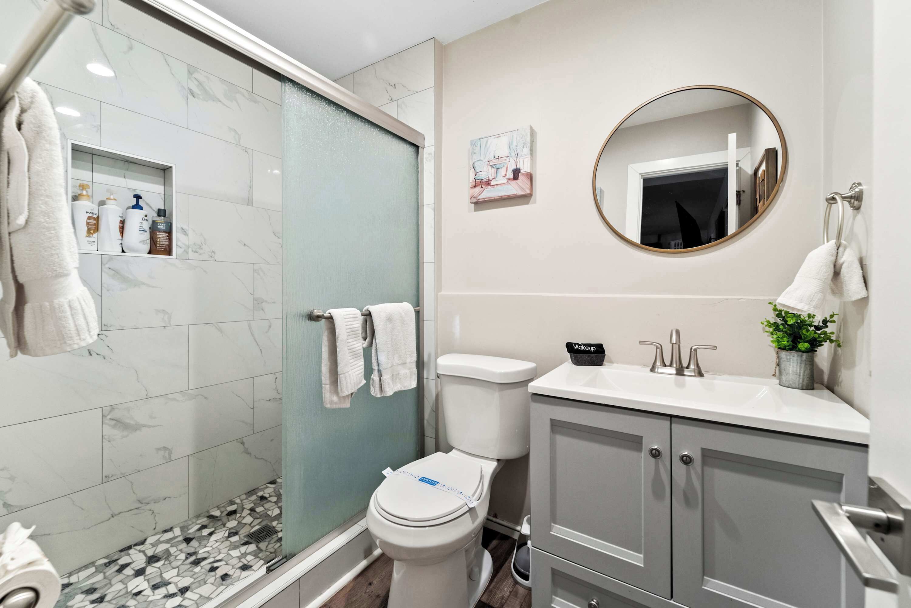 A modern bathroom with a glass shower enclosure, a toilet, a sink with a mirror, and a cabinet.