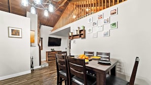 Un comedor con una mesa de madera, sillas y un televisor instalado en la pared.