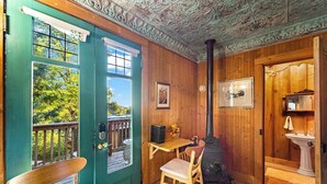 A cozy cabin interior with a wooden door, a small table with a chair, a fireplace, and a window with a view of trees. - Escape to Rustic Studio | Fireplace + Modern Comfort (Julian)