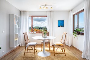 A room with a round table, two wicker chairs, a bookshelf, a window with a view, and a ceiling light fixture.