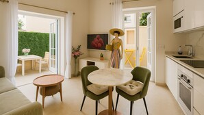 A modern living room with a round table, two green chairs, a sofa, and a kitchen area with a microwave and sink.