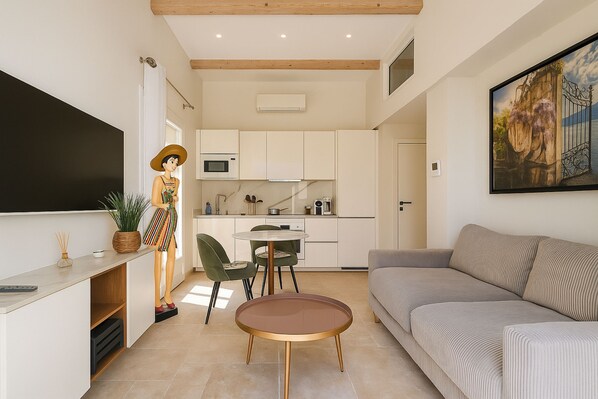 A modern living room with a sofa, a round table, and a kitchen area with cabinets and a TV.
