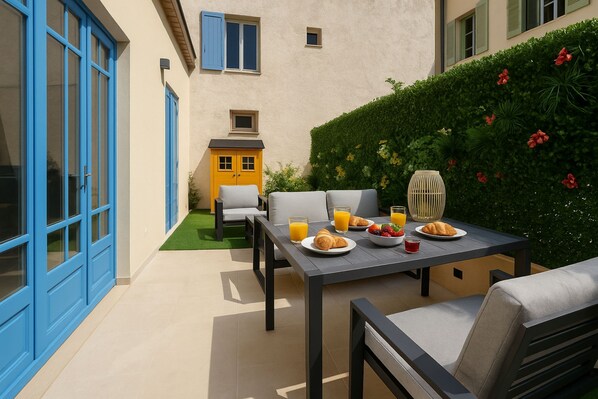 An outdoor patio with a table set for breakfast, including croissants, fruit, and orange juice.