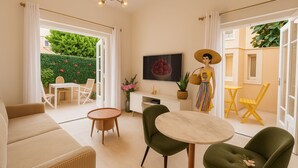 A modern living room with a sofa, two chairs, a small table, a TV, and a painting of a fruit bowl.
