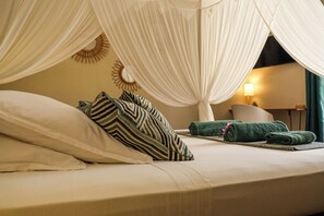 A bed with a canopy, pillows, a rolled-up towel, and a lamp in a room.