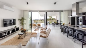 Un soggiorno moderno con televisione a schermo piatto, un'ampia finestra e un'area pranzo con sedie in vimini.
