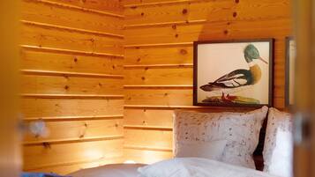 A wooden-paneled room with a bed, pillows, and a framed picture of a bird on the wall.