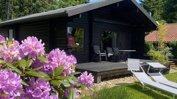 Eine Hütte mit einer Terrasse, Sitzgelegenheiten im Freien und einem Garten mit violetten Blumen.