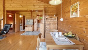A wooden cabin interior with a dining table set, a sofa, and a TV in the background.