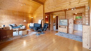 A log cabin interior with a living area, sofa, armchair, and a television.