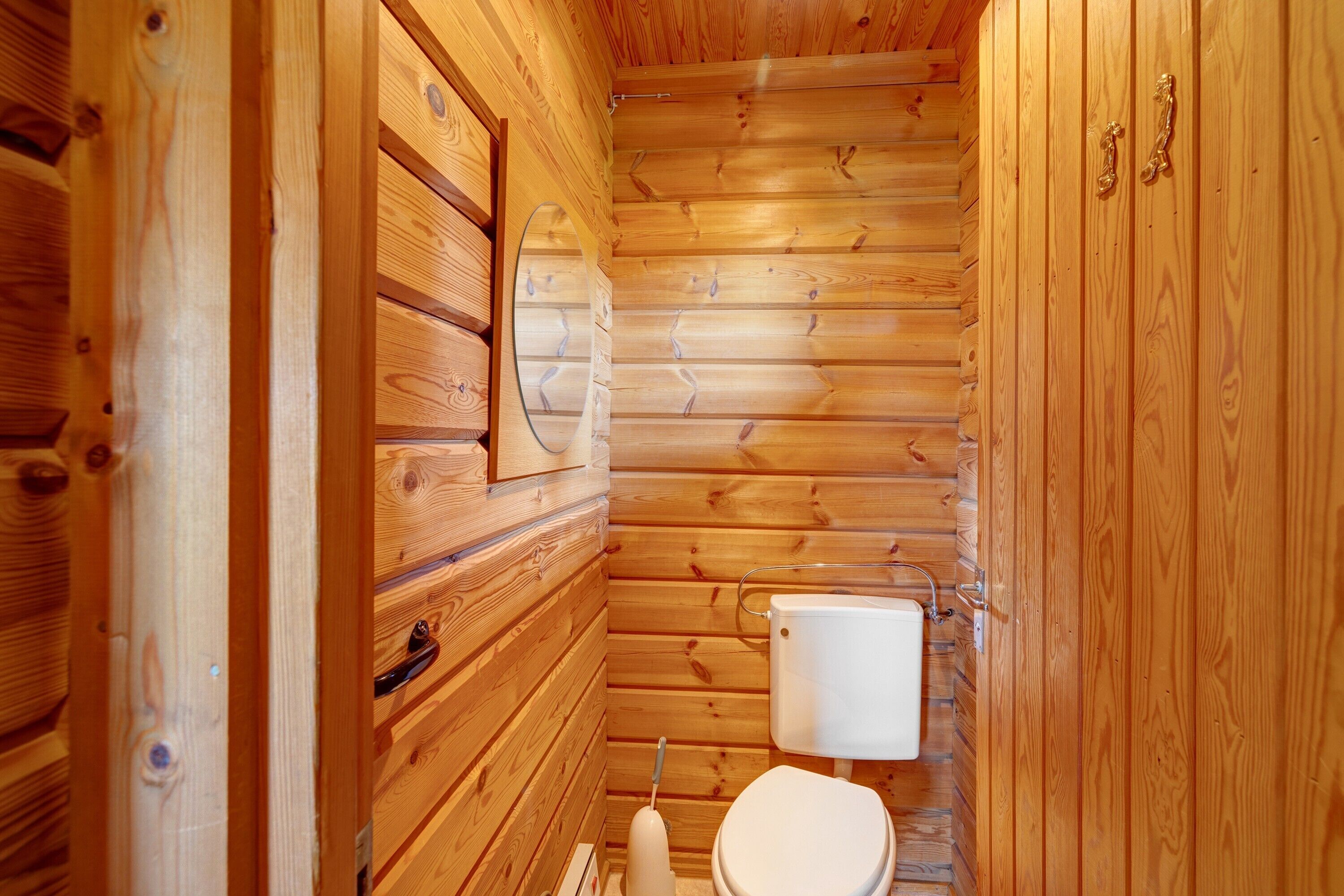L’intérieur d’une cabane en bois, avec un mur en bois, des toilettes blanches et une porte en bois.