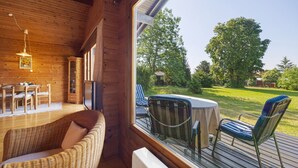 A wooden interior with a dining area, wicker sofa, and a view of a grassy yard through a large window.