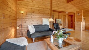 A log cabin interior with a sofa, armchairs, a coffee table, and a lamp.
