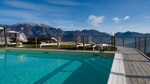 En pool med krystalklart blåt vand, omgivet af liggestole og parasoller, med et bjerg i baggrunden.