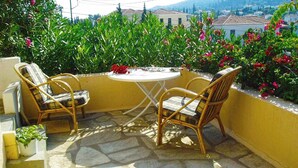 A patio with two wicker chairs and a small round table, surrounded by a yellow wall and stone flooring.