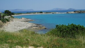 A coastal landscape with a clear blue sea, sandy beach, and distant mountains.