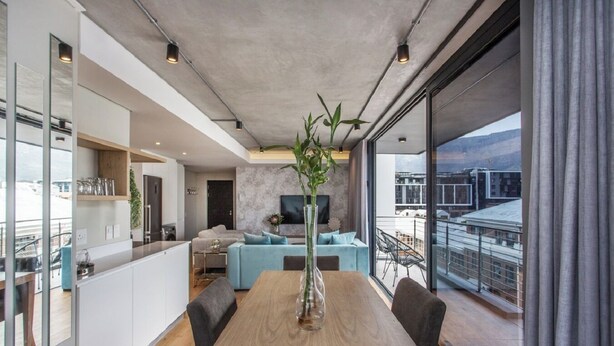 Ein modernes Wohnzimmer mit Essbereich, großen Fenstern und Blick auf Gebäude.