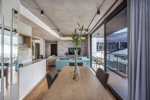 A modern living room with a dining area, large windows, and a view of buildings. - The Docklands 2 Bed Executive Apartment (Cape Town)