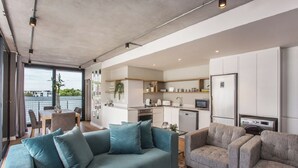 Ein modernes Wohnzimmer mit einer Couch und Sesseln, eine Küche mit weißen Schränken und ein Balkon mit Blick.