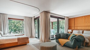 A modern hotel room with a large bed, a sofa, and a desk. There is a large window with curtains, and the room has a wooden headboard. - Clara Arte Resort (Brumadinho)