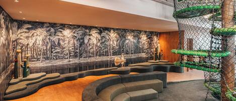 Un área lounge moderna con una disposición de asientos curvada, un mural de palmeras y una estructura de juegos vertical.