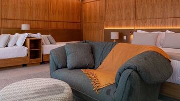 Una habitación de hotel moderna con cabecera de madera, un sofá, una cama y una mesita de noche con lámpara.