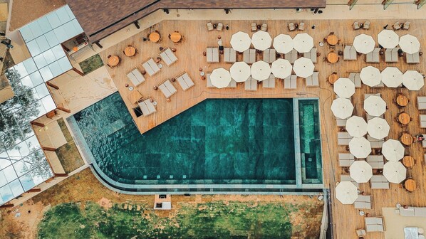 An aerial view of a resort with a large swimming pool, multiple sun loungers, and outdoor seating areas.
