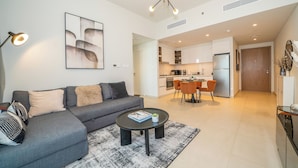 A modern living room with a grey sofa, a coffee table, and a dining area with orange chairs. - Zapbed House-DT 2103 (Dubai)